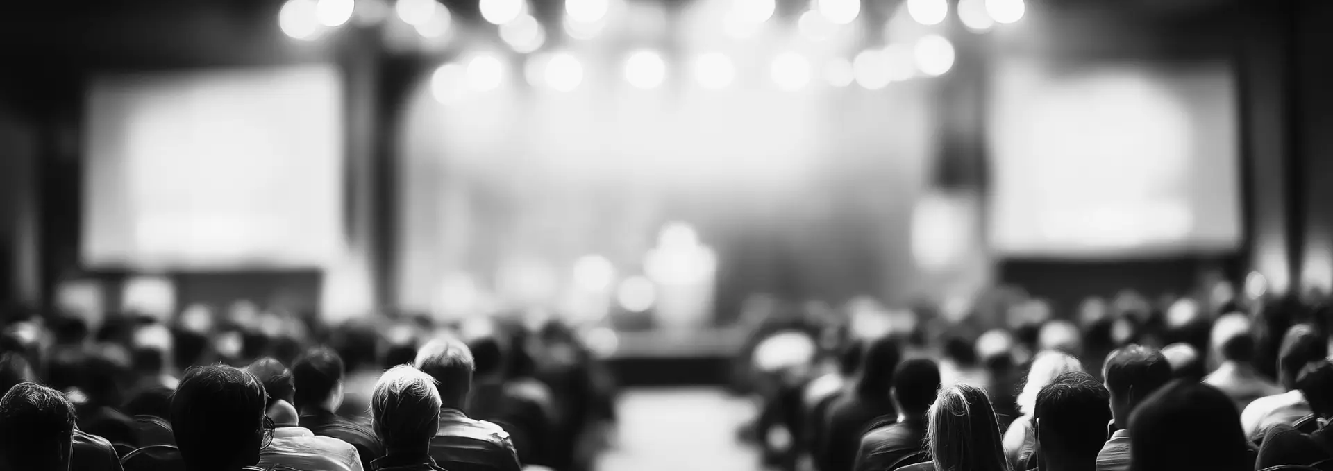 Packed conference hall, audience seen from behind facing the stage